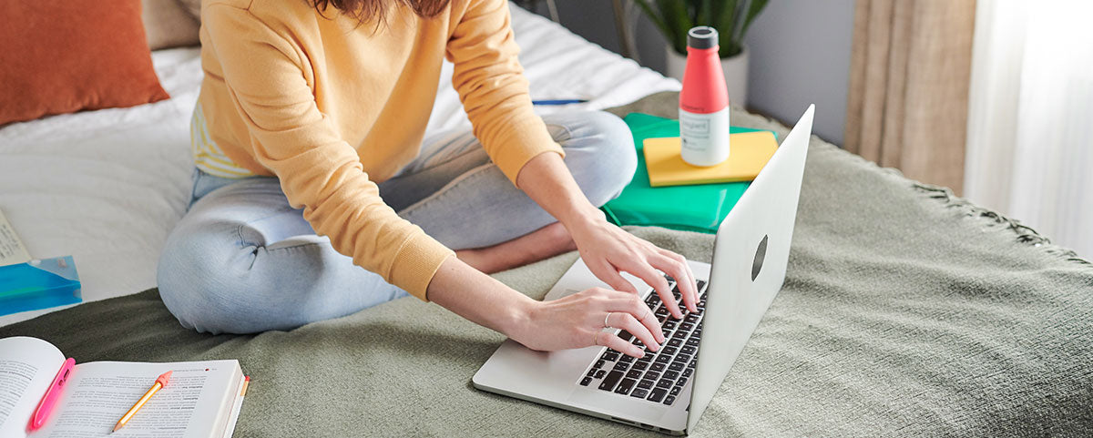 Student sitting on bed typing on a laptop