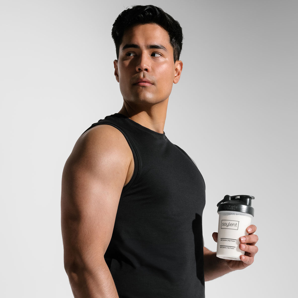 Athletic man holding vanilla Soylent Complete Protein Powder shake in a Soylent blender bottle.